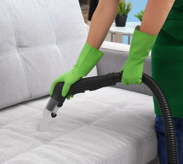 Person steam cleaning gray sofa